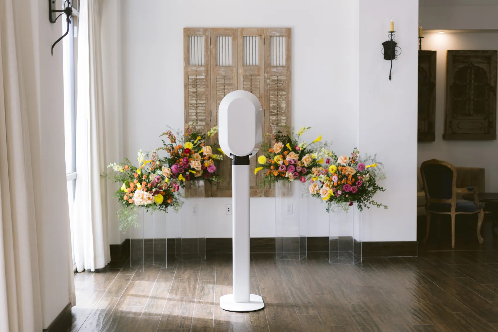 The booth standing in front of a long low arrangement of pink, orange and yellow flowers against a white wall