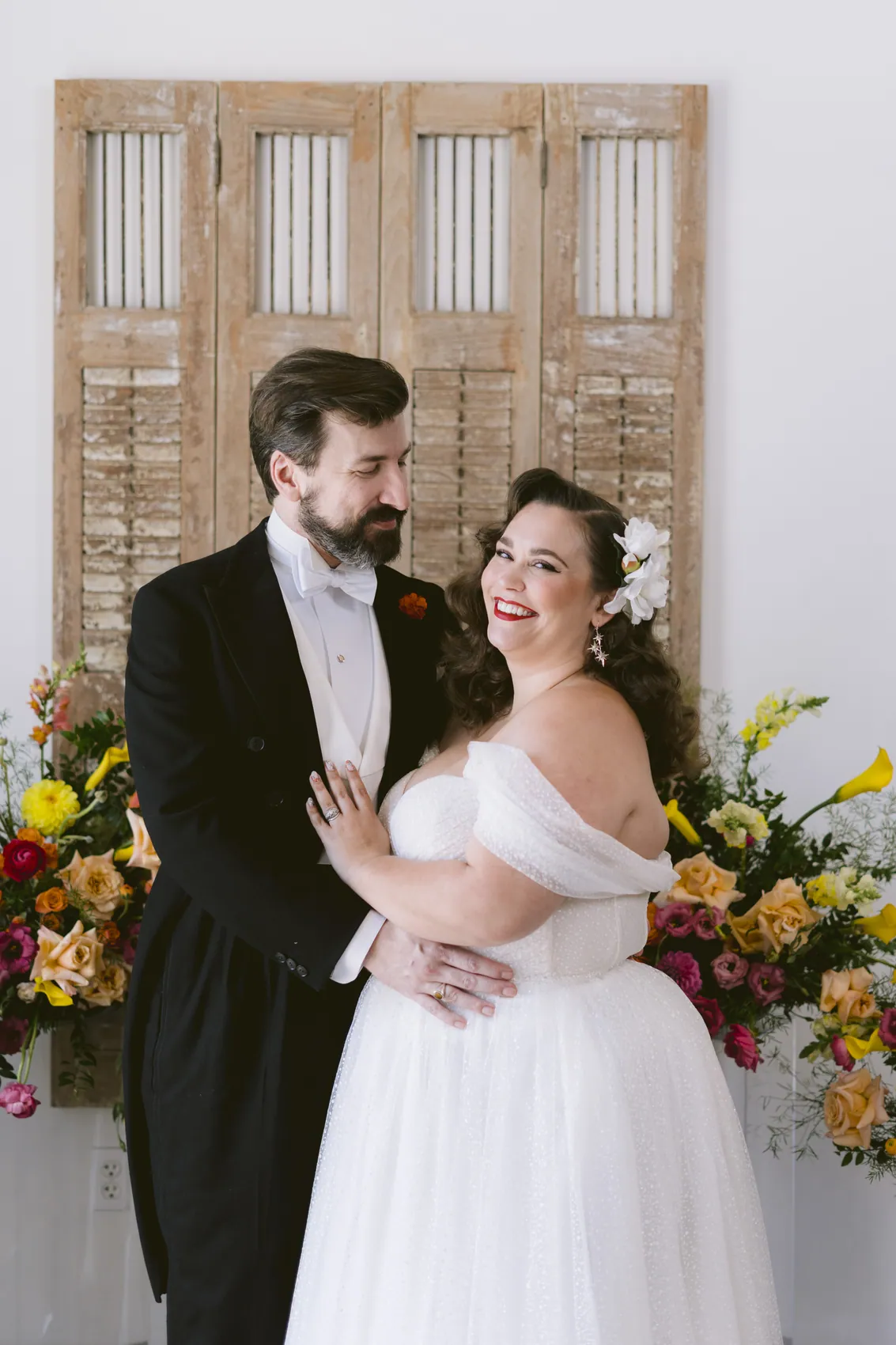 A bride and groom laughing together in front of a bright floral wall