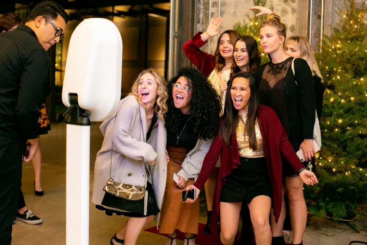 A group of guests laughing at the booth beside a lit Christmas tree