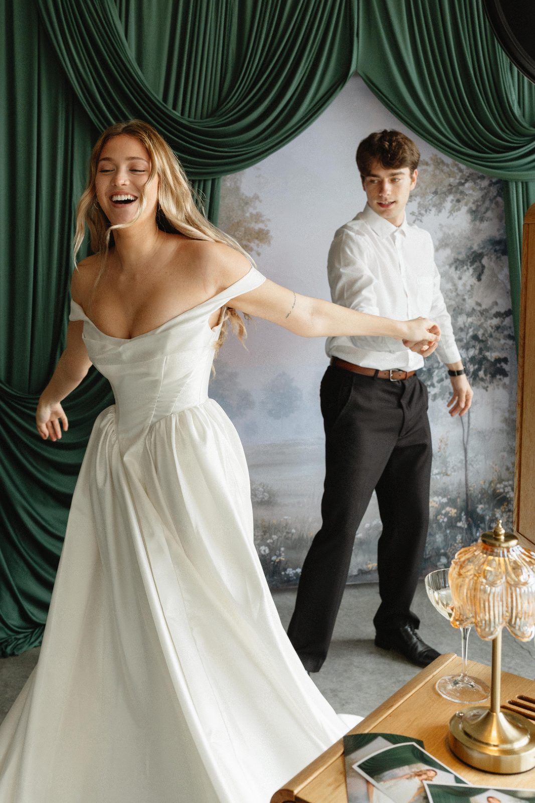 A bride laughing as she turns in her gown in front of heavy green velvet drapes and a painted backdrop