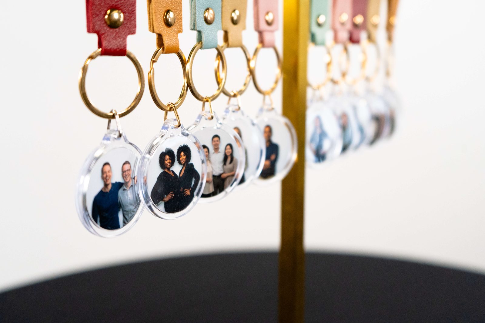 Clear round photo keychains hanging in a row from gold rings with pastel leather tabs